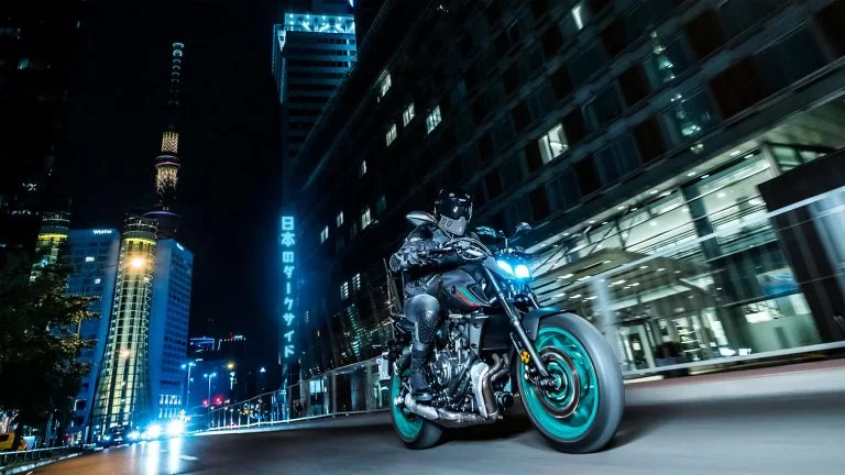 zwarte Yamaha MT-07 met turquoise velgen te zien vanuit het vooraanzicht rijd in het donker door een verlichte stad