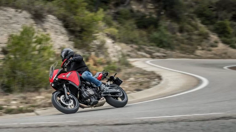 rode Yamaha Tracer 7 rijd door een s-bocht te zien vanuit het zijaanzicht met als achtergrond een rotsachtige omgeving