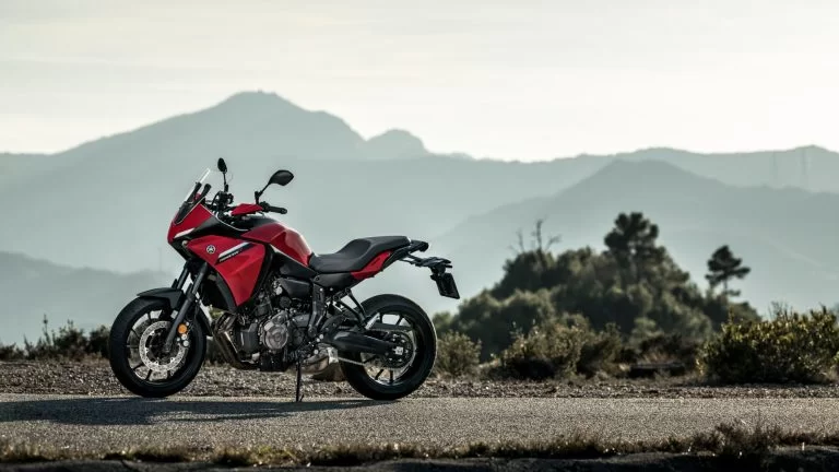 rode Yamaha Tracer 7 staat bovenop een berg weg te zien vanuit het zijaanzicht met als achtergrond bergen