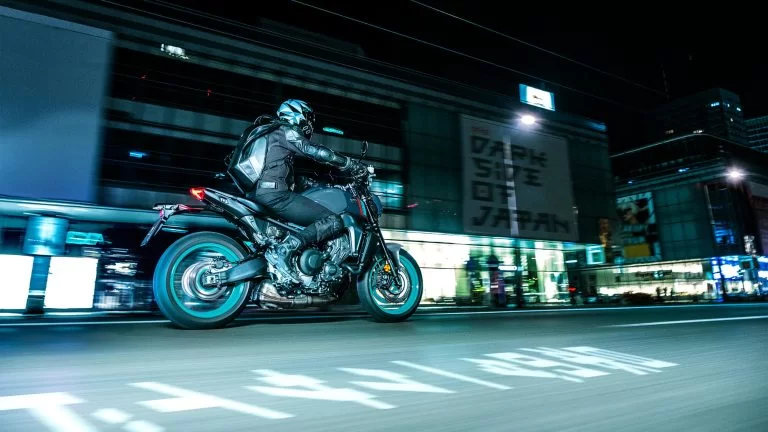 zwarte Yamaha MT-09 met turquoise velgen rijd in het donker door een verlichte stad te zien vanuit het zijaanzicht