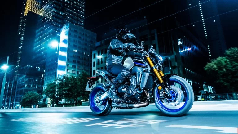 grijs met zwarte Yamaha MT-09 SP met blauwe velgen rijd door het donker in een verlichte stads omgeving te zien vanuit het zijaanzicht