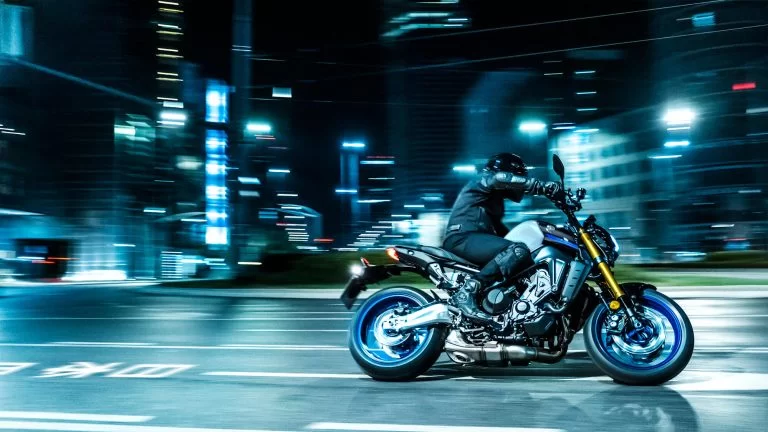 grijs met zwarte Yamaha MT-09 SP met blauwe velgen rijd in het donker door een bocht in de stad te zien vanuit het zijaanzicht met gebouwen op de achtergrond