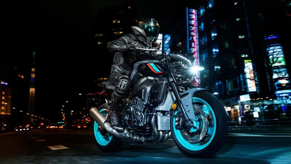 zwarte Yamaha MT-10 met turquoise velgen rijd in het donker met een verlichte stad op de achtergrond te zien vanuit het voorzijaanzicht