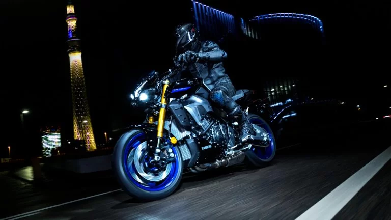 zwarte Yamaha MT-10 SP met blauwe velgen rijd in het donker met een verlichte toren op de achtergrond te zien vanuit het voorzijaanzicht