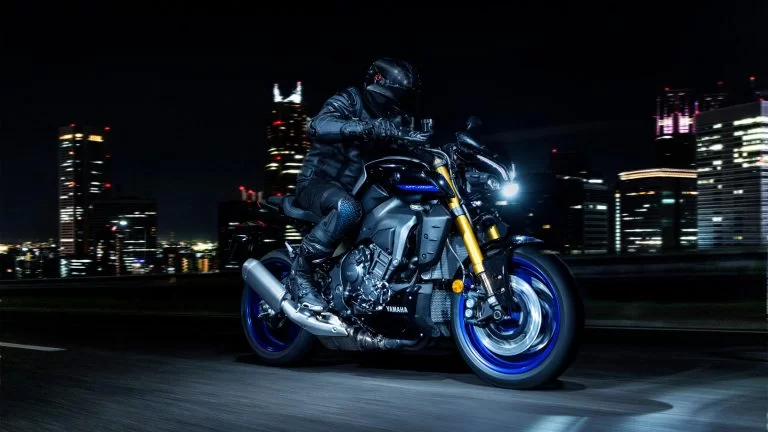 zwarte Yamaha MT-10 SP met blauwe velgen rijd in het donker met een verlichte stad op de achtergrond te zien vanuit het voorzijaanzicht