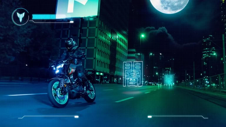 zwarte Yamaha MT-125 met turquoise velgen rijd in het donker door een verlichte stad met de maan op de achtergrond te zien vanuit het voorzijaanzicht