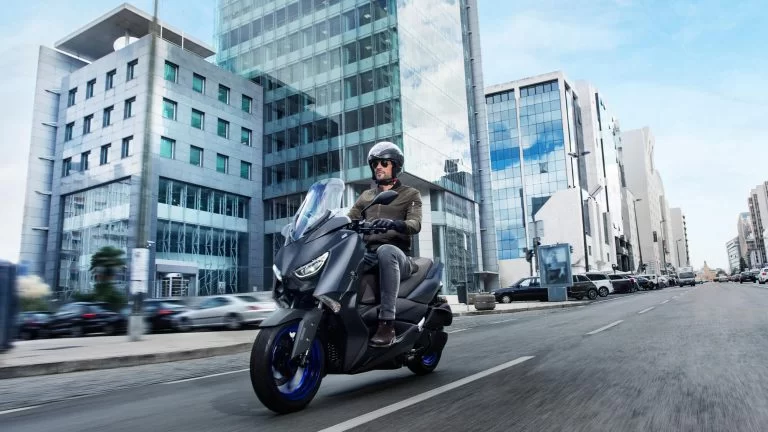Actiefoto 2022-Yamaha-XMAX300-EU-Icon_Blue-Static-001-03 vooraanzicht met motorrijder die door de stad rijdt.