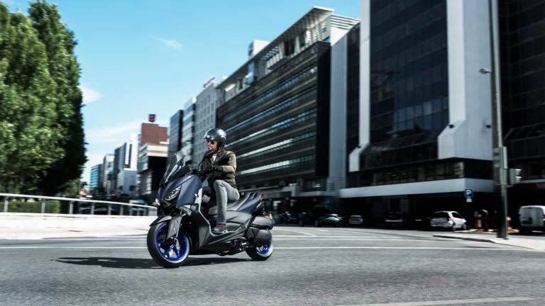 Actiefoto 2022-Yamaha-XMAX300-EU-Icon_Blue-Static-001-03 zijaanzicht met motorrijder die de bocht omgaat in de stad.
