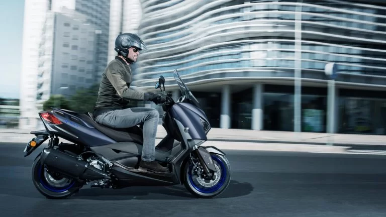 Actiefoto 2022-Yamaha-XMAX300-EU-Icon_Blue-Static-001-03 zijaanzicht met motorrijder die door de stad rijdt.
