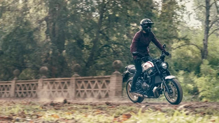 Actiefoto 2022-Yamaha-XS700SCR-EU-Tech_Black-Action-004-03 op afstand in bosrijke omgeving met motorrijder die op z'n voetstukken staat