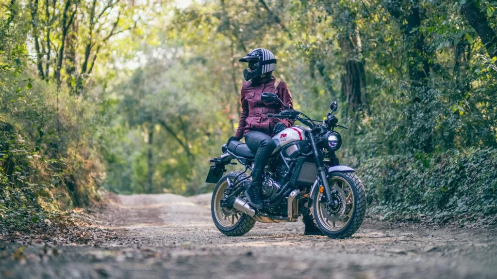 Actiefoto 2022-Yamaha-XS700SCR-EU-Tech_Black-Action-004-03 in bosrijke omgeving met motorrijder die naar de zijkant het bos inkijkt
