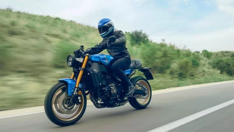 Actiefoto 2022-Yamaha-XS850-EU-Legend_Blue-Action-002-03 met motorrijder die over een weg langs heuvelachtig stuk groen rijdt