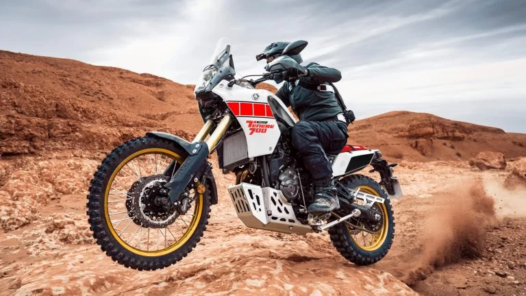 Actiefoto 2023 Yamaha Ténéré 700 zijaanzicht van onder genomen met motorrijder met voorwiel los komt van de grond in woestijnachtig gebied.