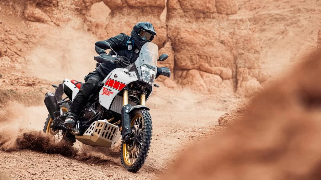 Actiefoto 2023 Yamaha Ténéré 700 vooraanzicht van motorrijder die gravel doet opstuiven door gas te geven in een off-road gebied met rotsen op de achtergrond