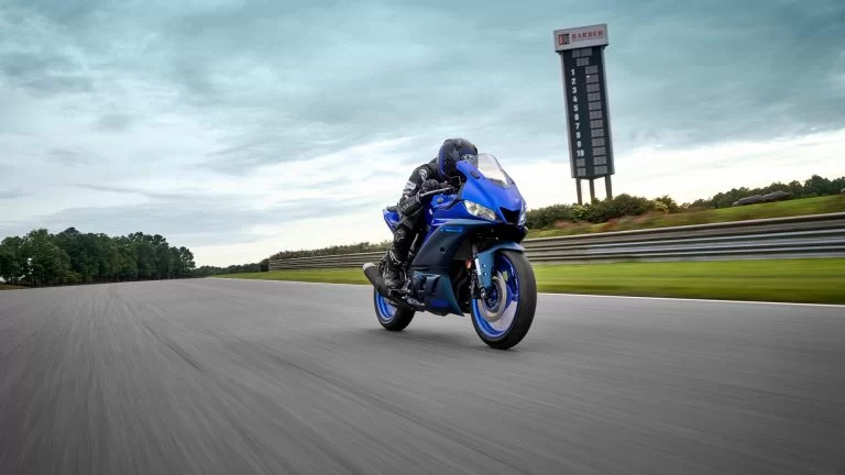 blauwe Yamaha YZF-R3 rijd op een circuit te zien vanaf het voorzijaanzicht met een bewolkte lucht op de achtergrond