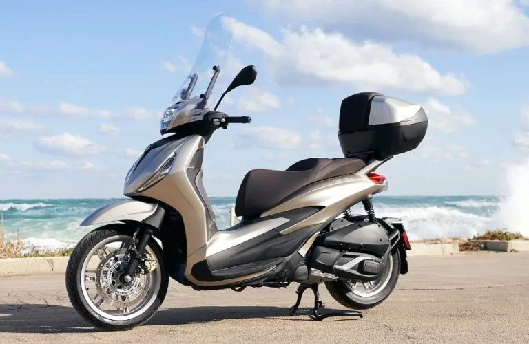 lifestylefoto met een 2023-piaggio-beverly-400-motorscooter en een golf die stukslaat op de kust op de achtergrond