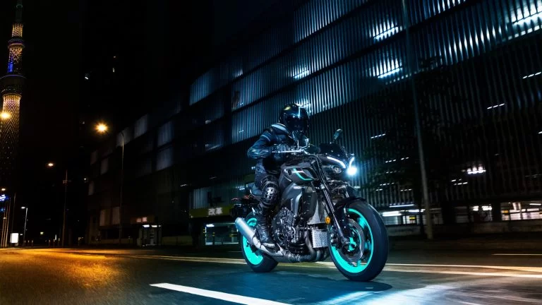 motorrijder rijdt langs een groot gebouw in de nacht op een mt-10 met felgekleurde cyan velgen