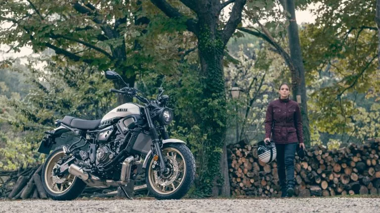 vrouwelijke motorrijder loopt met de helm in de hand naar haar sport Heritage motor toe die in het bos staat