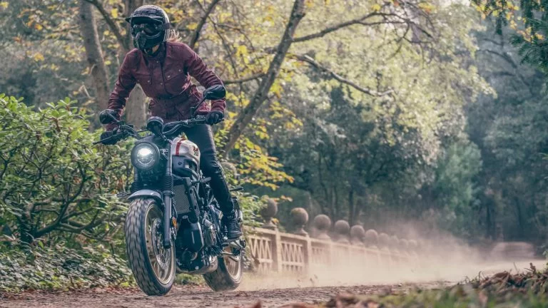 motorrijdster rijdt over een onverharde weg door een bos op een sport Heritage motor