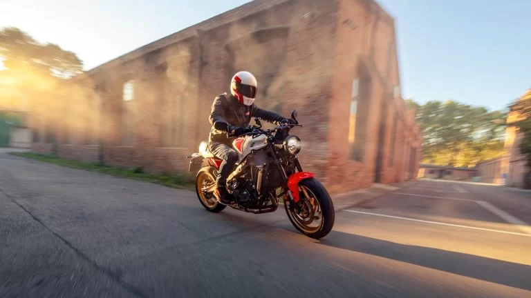 Motorrijder rijdt over een terrein met gebouwen op een sport Heritage motor
