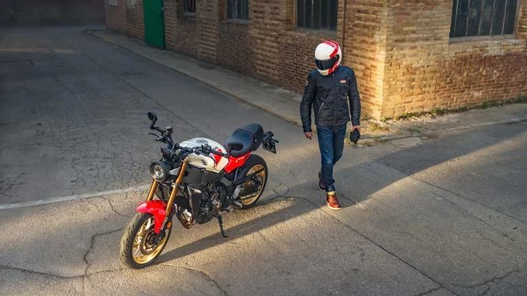 Motorrijder staat naast zijn urban sport Heritage motor op een terrein met een gebouw