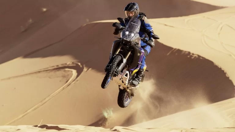 Adventure motor met motorrijder die los van de grond komt met de motor in de woestijn met duinen op de achtergrond