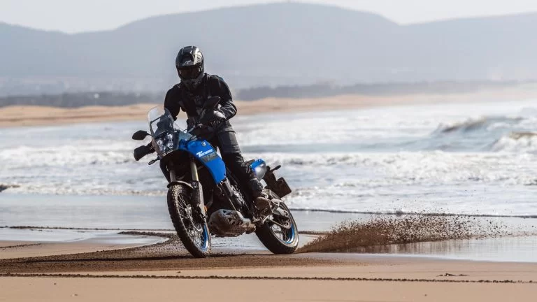 Motorrijder rijdt op een blauwe adventure motor door een plas water in de woestijn