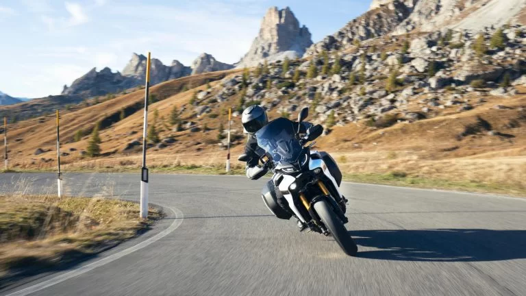 motorrijder rijdt op een sport tour motor door een bocht te zien vanaf de voorkant met heuvels en bergen op de achtergrond