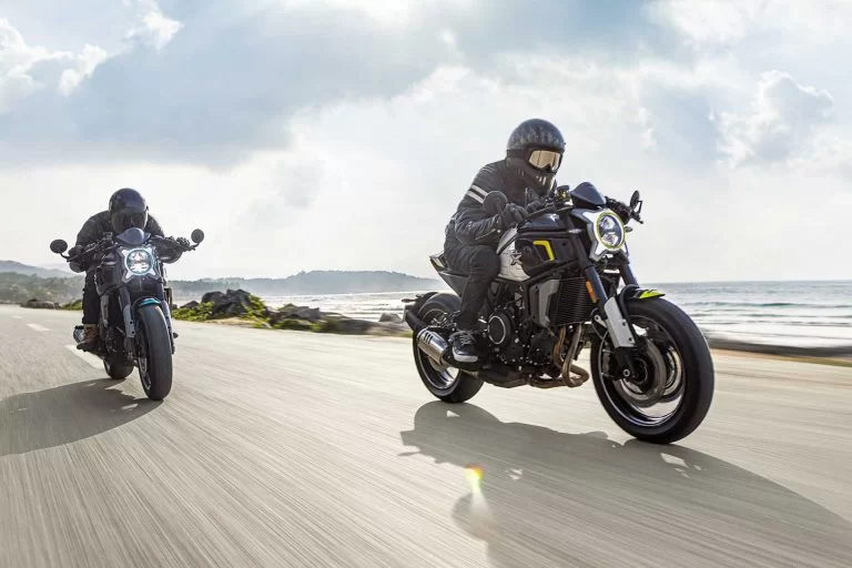 Actiefoto twee CF Moto's 700CL-X SPORT parelwit met motorrijders en kustlijn op de achtergrond