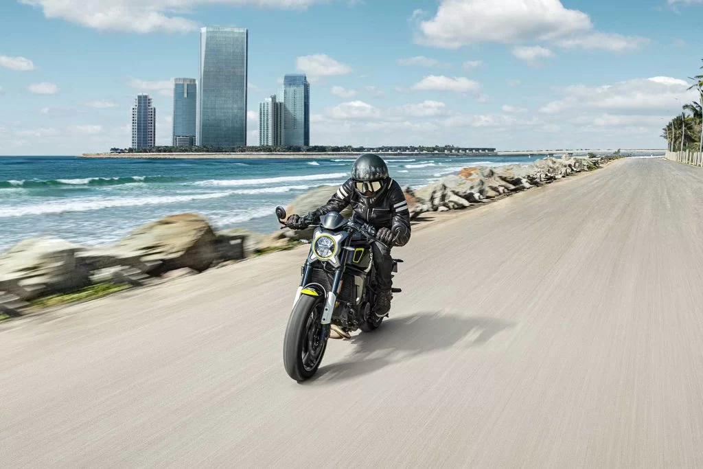 Productfoto CF Moto 700CL-X SPORT parelwit met motorrijder en stad en kustlijn op achtergrond