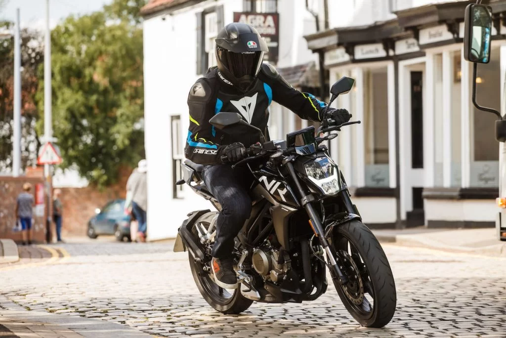 CF Moto 300nk actiefoto motorrijder die met bocht neemt en in dorp