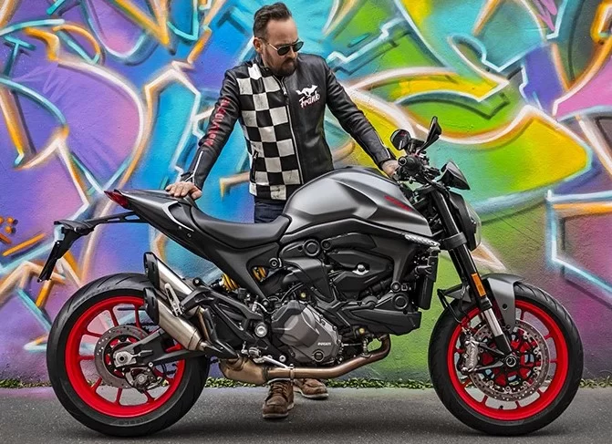 Man die staat bij een Ducati Monster Naked bike met een graffiti muur op de achtergrond