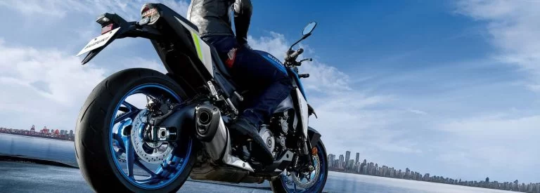 Lifestylefoto 2023 Suzuki GSX-S1000 achteraanzicht van laag positie genomen met motorrijder op de motorfiets en blauwe lucht op de achtergrond