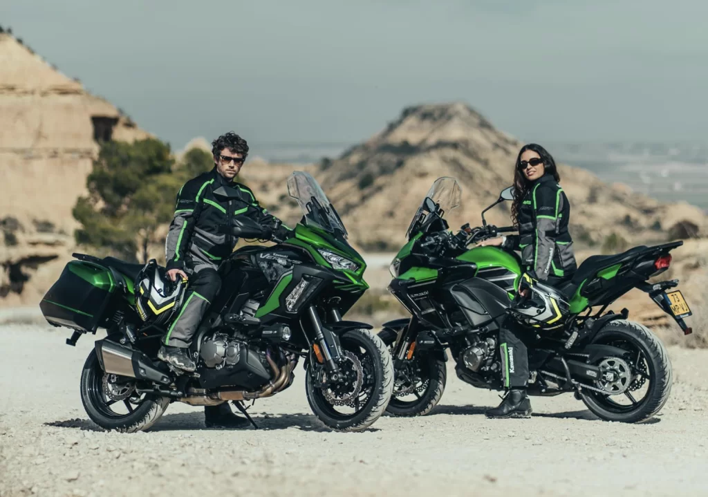 Lifestylefoto twee 2023 Kawasaki Versys 1000 S met motorrijders die in de camera kijken in een dor en heuvelachtig landschap