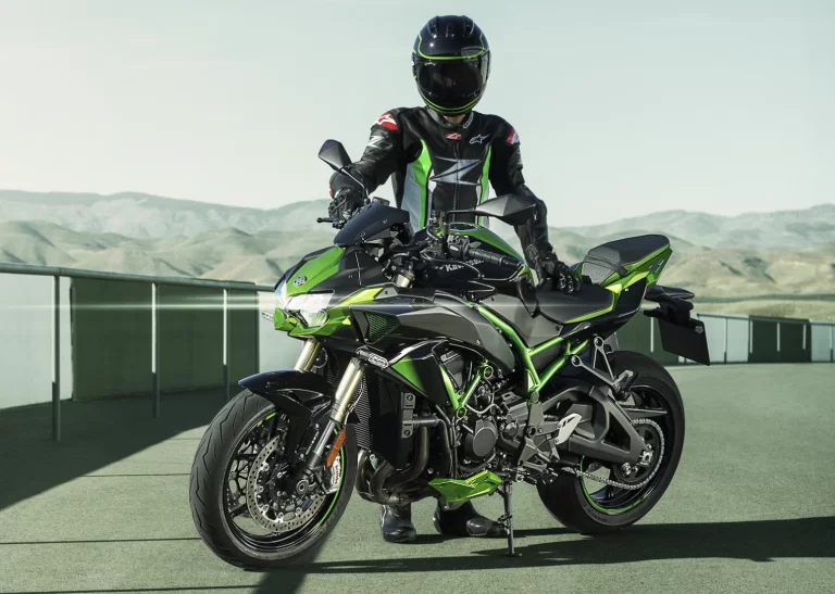 Lifestylefoto 2023 Kawasaki ZH2 SE groen schuin vooraanzicht op racecircuit. Motorrijder staat naast motorfiets en kijkt in de camera.