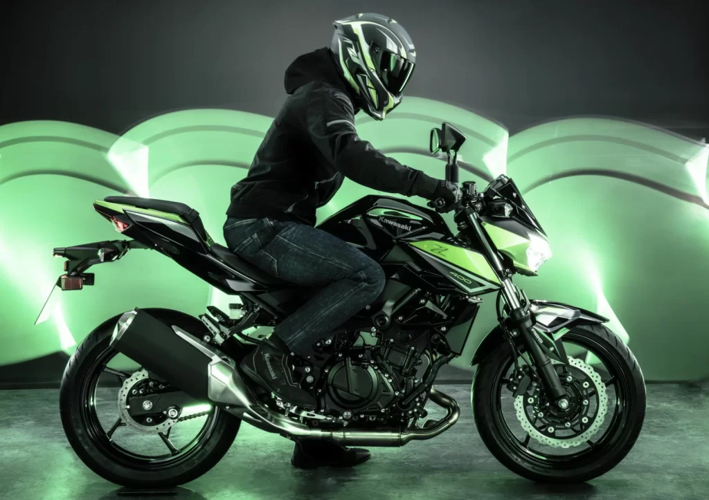 Studiofoto 2023 Kawasaki Z400 zijaanzicht met motorrijder zittend op het zadel en groene sfeerverlichting.