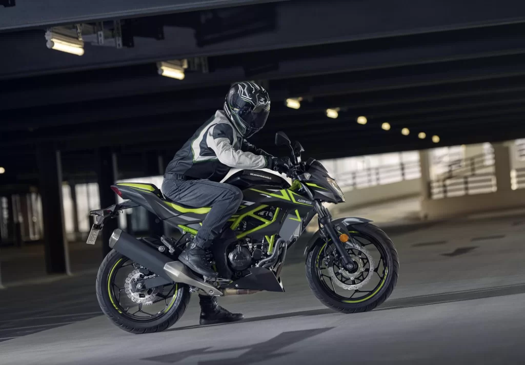 Lifestylefoto 2023 Kawasaki Z125 zijaanzicht met motorrijder voorover leunend op stuur in parkeergarage.
