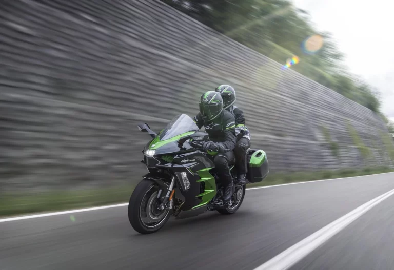 Actiefoto Ninja H2 SX schuin vooraanzicht met motorrijder en passagier die langs een muur rijden