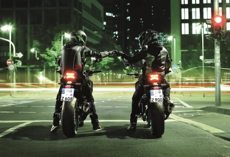 Lifestylefoto 2023 Kawasaki Z900 70kW met twee motorrijders die elkaar in de avonduren een boks geven in de stad