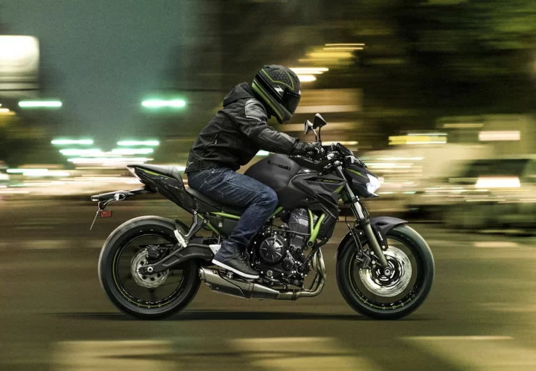Actiefoto 2023 Kawasaki Z650 zijaanzicht met motorrijder die snel rijdt in stedelijk gebied in avonduren.