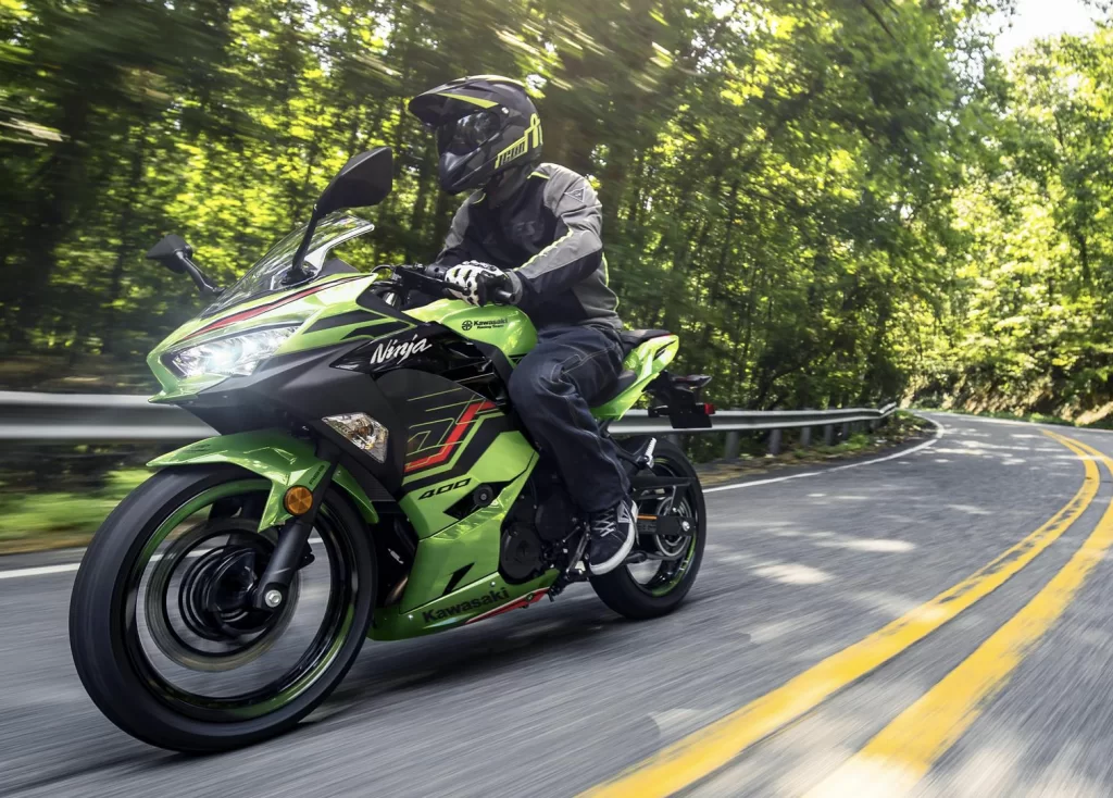 Actiefoto 2023 Kawasaki Ninja 400 met motorrijder op weg in bosrijke omgeving