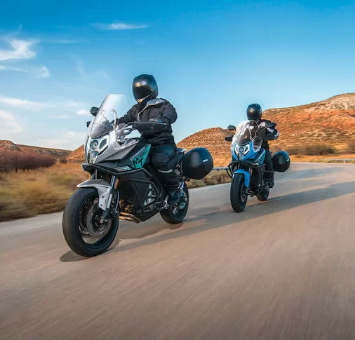 Actiefoto van twee motorrijders op een CF Moto 650 MT met aanzicht schuin van voren in heuvelachtig landsschap.