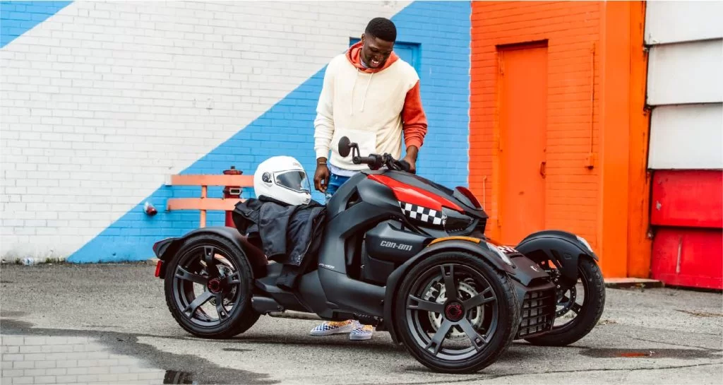 zwart met rode Can-Am Ryker 600 te zien vanuit het zijaanzicht met op de achtergrond een oranje met blauw en wit gebouw