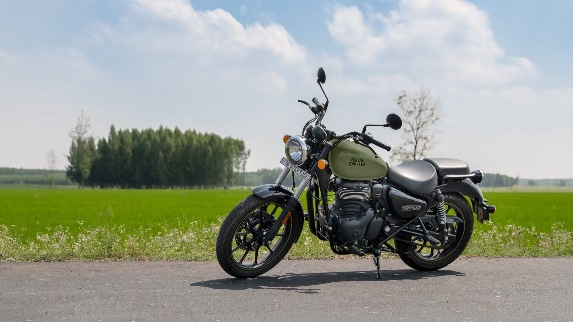 Groene Royal Enfield's Meteor 350 met groen veld en blauwe bewolkte lucht op de achtergrond