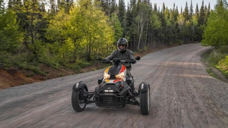zwart met geel en rode Can-Am Ryker Sport 900 rijdend over een grindpad met als achtergrond een bosrijke omgeving