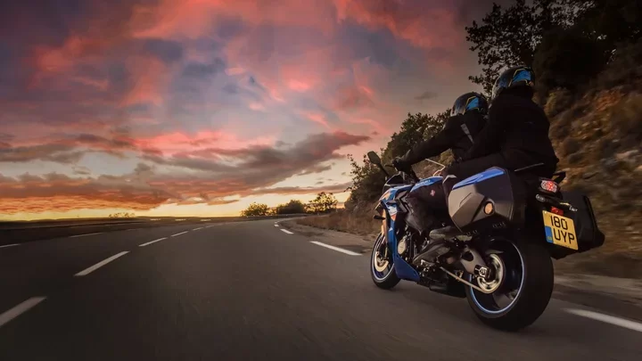 Blauwe Suzuki motor rijdend op straat rijder en passagier.