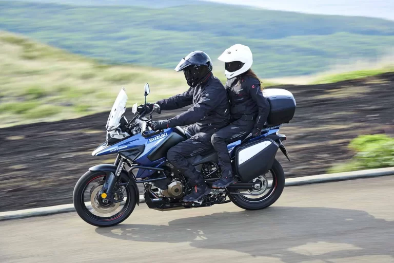 Suzuki tourmotor rijdend over straat met rijder en passagier.