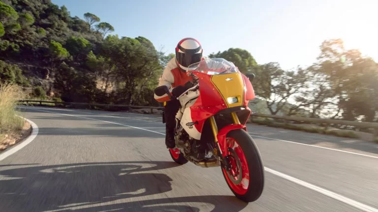 Motorrijder rijdt op een rood met gele sport Heritage gp motor in een bergachtige omgeving